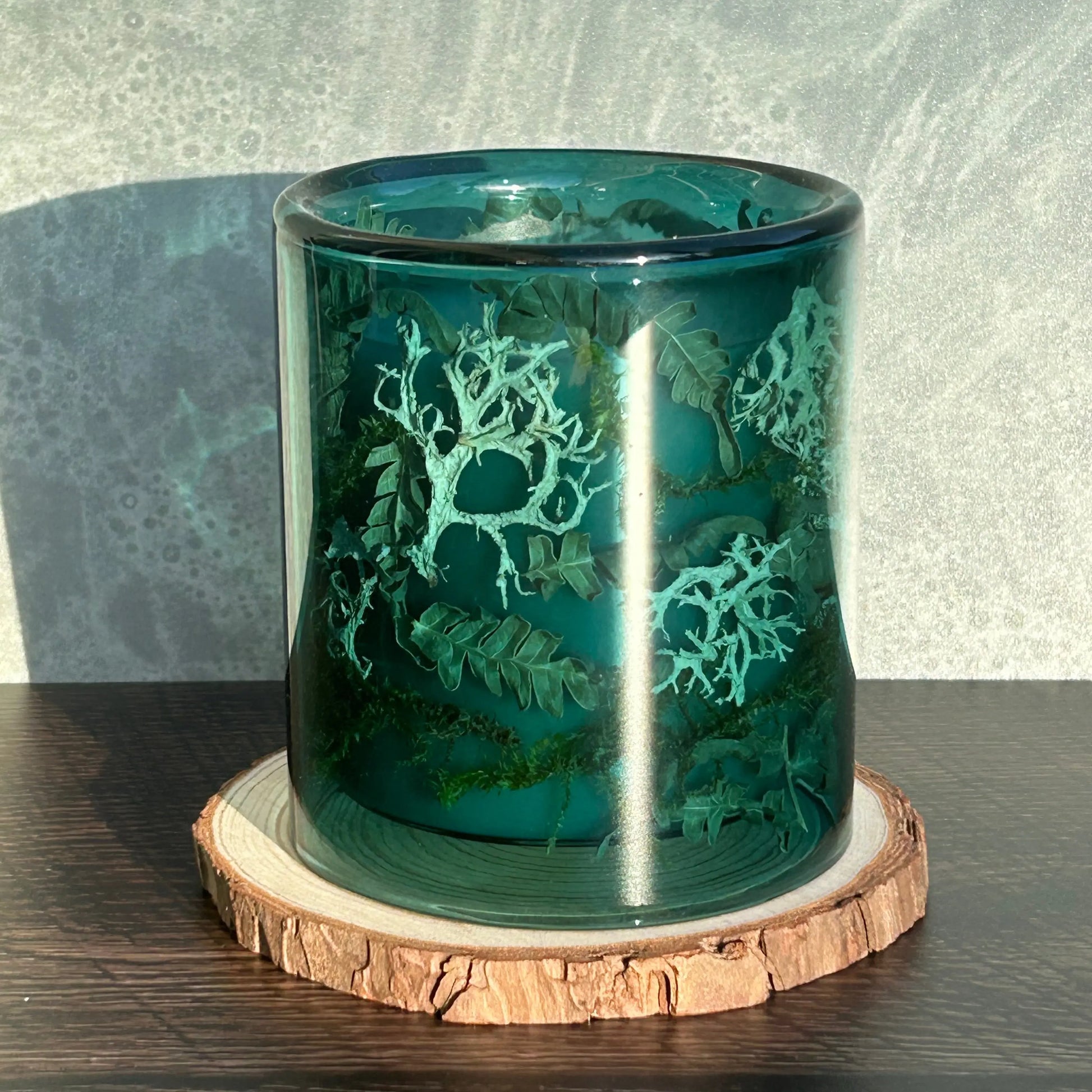 Candle in a see-through blue jar on top of a circle of wood.