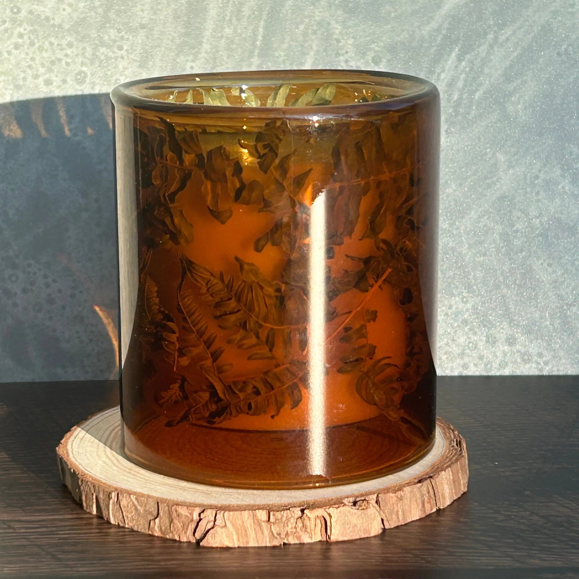 Candle in a see-through orange jar with flowers and greenery placed inside the jar.