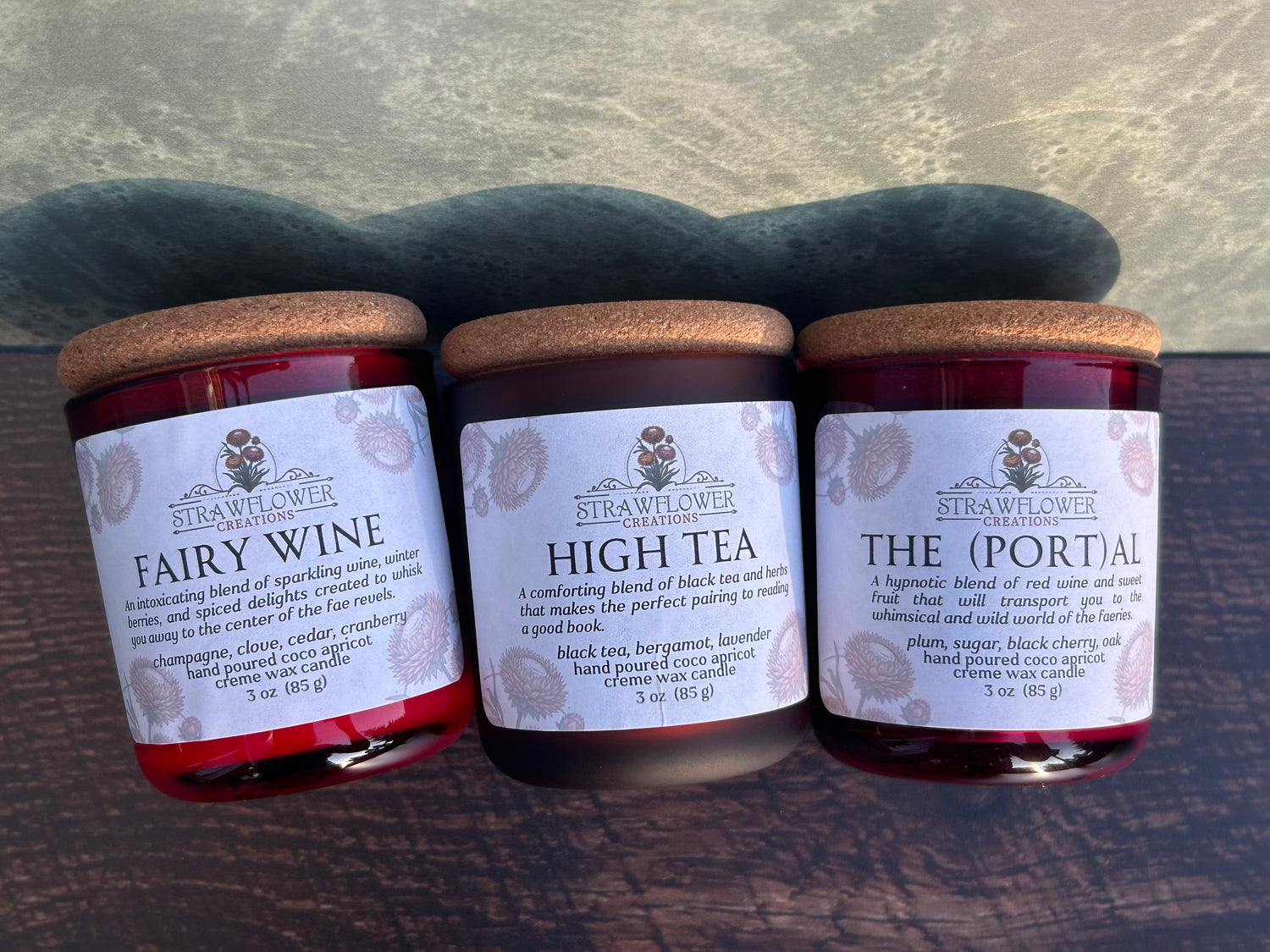 Three candles in red jars laying side by side on a table with cork tops